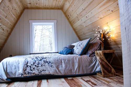 Cozy bedroom with wooden walls, a bed adorned with floral bedding, and a small wooden side table with a decorative lamp.