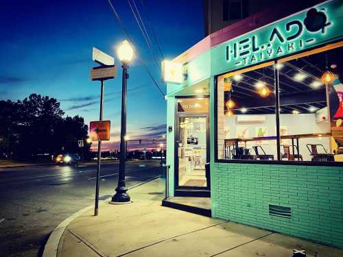 A colorful restaurant exterior at dusk, with a street sign and lamppost nearby, creating a vibrant urban scene.