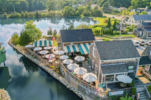 Aerial view of a waterfront restaurant with outdoor seating, umbrellas, and lush greenery surrounding a calm waterway.