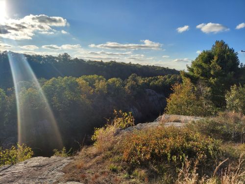 A scenic view of a rocky landscape with trees and a blue sky, featuring sunlight streaming through the clouds.