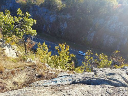 A view from a rocky ledge overlooking a winding road surrounded by trees and autumn foliage.