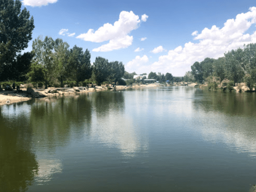 A calm river surrounded by trees and rocks under a blue sky with fluffy clouds.