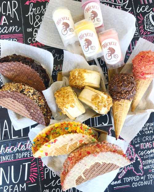 A colorful assortment of ice cream treats, including waffle tacos, cones, and popsicles, on a chalkboard background.