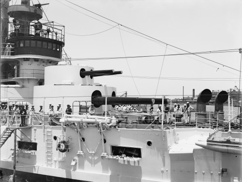 A historic naval ship with large cannons, crew members on deck, and a clear sky in the background.