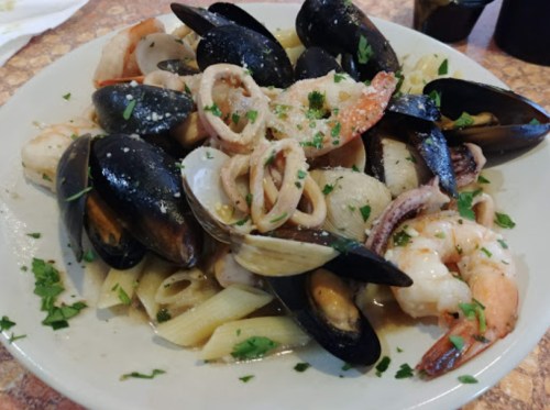 A plate of seafood pasta featuring shrimp, mussels, clams, and squid, garnished with parsley.