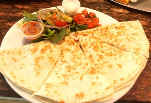 A plate of quesadillas cut into wedges, served with a side salad, salsa, and a small cup of sauce.