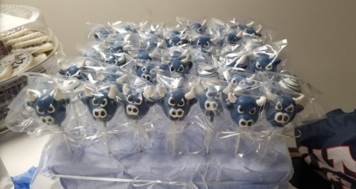 A display of blue cake pops shaped like cow heads, wrapped in clear plastic with white ribbons.