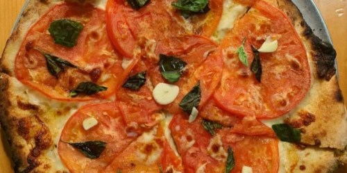 A freshly baked pizza topped with sliced tomatoes, fresh basil, and garlic on a golden crust.