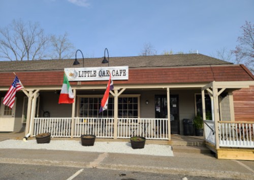 Exterior of Little Oak Cafe featuring flags, a porch, and a welcoming entrance on a clear day.