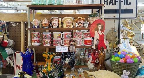 A display of vintage items including mugs, figurines, and glassware, with a red dress cutout and colorful Easter eggs.