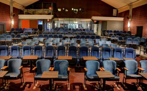 A spacious auditorium with rows of blue chairs and tables, set up for an event or presentation.