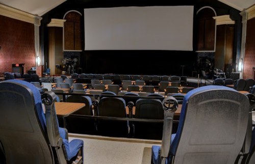 A nearly empty cinema with blue seats facing a large blank screen.