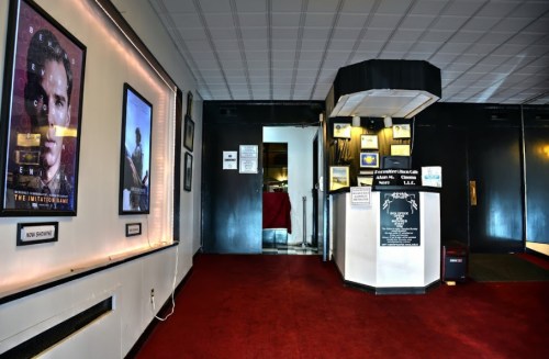 Interior of a movie theater featuring red carpet, posters on the wall, and a ticket booth at the entrance.