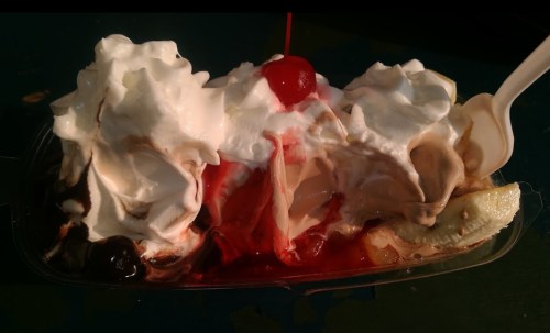 A dessert with layers of ice cream, whipped cream, cherries, and chocolate syrup in a plastic dish.
