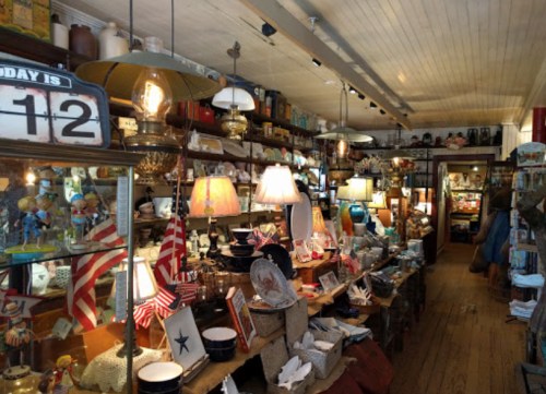 A cozy vintage shop filled with various antiques, lamps, and decorative items, featuring warm lighting and wooden shelves.
