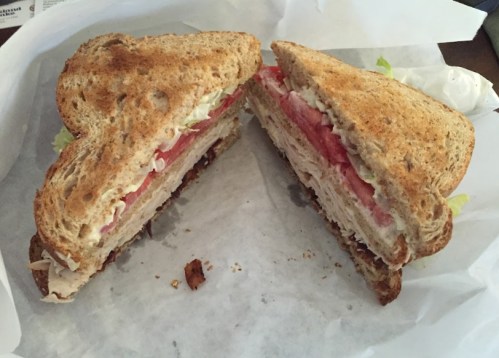A toasted sandwich cut in half, filled with turkey, lettuce, and tomato, served on a white paper wrapper.
