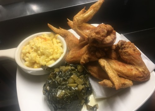 A plate of crispy fried chicken wings, macaroni and cheese, and collard greens.