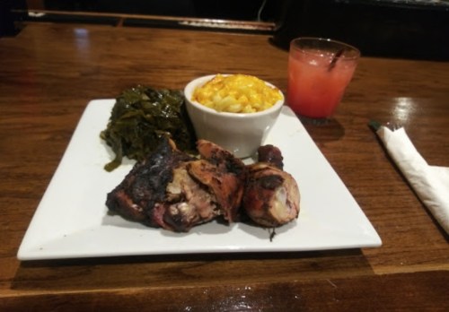 A plate with grilled chicken, collard greens, and macaroni and cheese, alongside a small glass of pink drink.