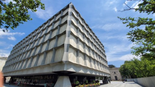 Modern concrete building with a textured facade, surrounded by trees and a clear blue sky.