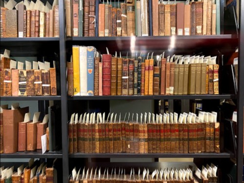 A wooden bookshelf filled with various old books, some with spines visible and others partially hidden.