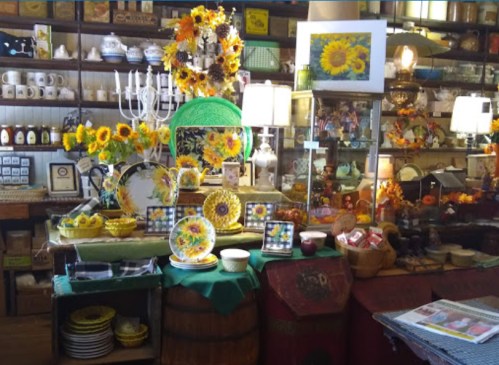 A cozy shop display featuring sunflowers, colorful plates, and various decorative items on wooden shelves.