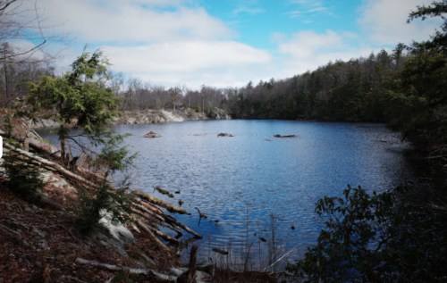 A serene lake surrounded by trees and rocky terrain under a partly cloudy sky.