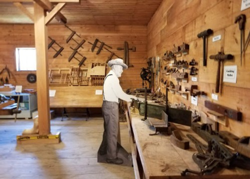 A vintage workshop with wooden walls, tools displayed, and a figure examining equipment at a workbench.