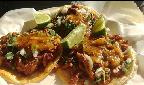 Three tacos filled with meat, topped with salsa, onions, and cilantro, served with lime wedges on a white plate.