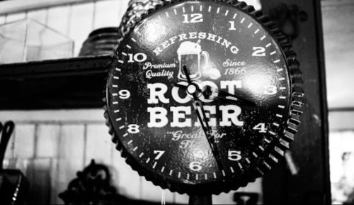 A vintage black and white clock featuring "Root Beer" and a beer mug design, hanging on a wall.