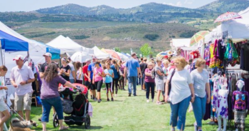A bustling outdoor market with colorful tents, vendors, and a crowd of people enjoying the sunny day.