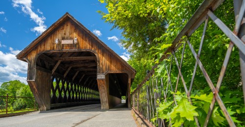 A wooden covered bridge surrounded by greenery under a bright blue sky.