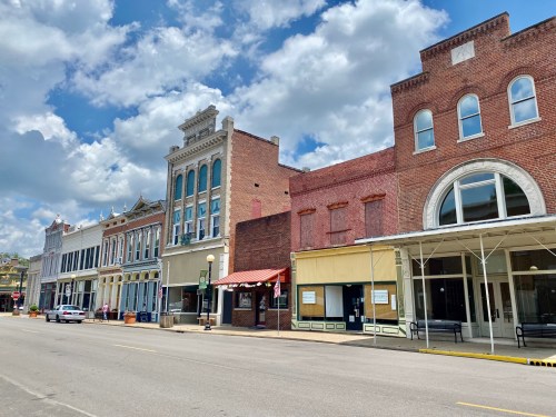 Historic buildings line a quiet street under a partly cloudy sky, showcasing classic architecture and storefronts.