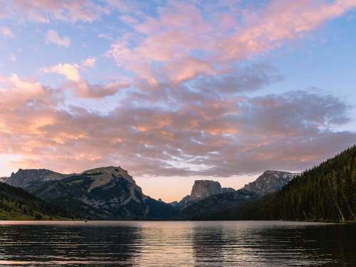 Scenic view of a lake surrounded by mountains under a colorful sunset sky with clouds.