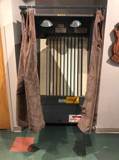 A vintage jukebox with curtains on either side, displayed in a museum or retro setting.