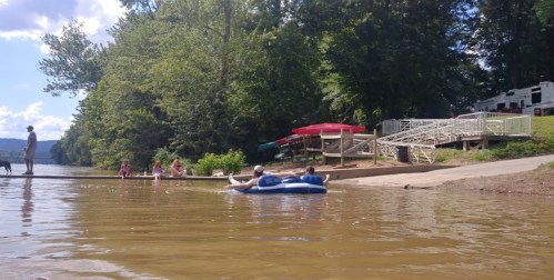 A group of people enjoying a sunny day by the lake, with some on a dock and others in a blue inflatable raft.