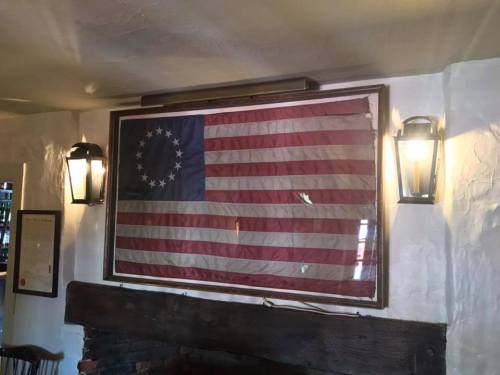 A historic American flag displayed on a wall, flanked by two lanterns in a rustic setting.