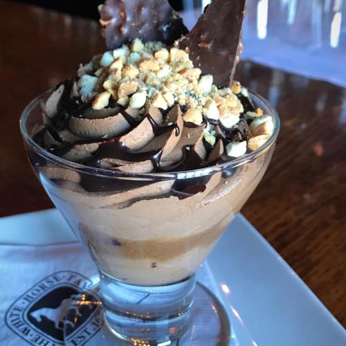 A dessert in a glass featuring chocolate mousse, topped with crushed nuts and chocolate shards.