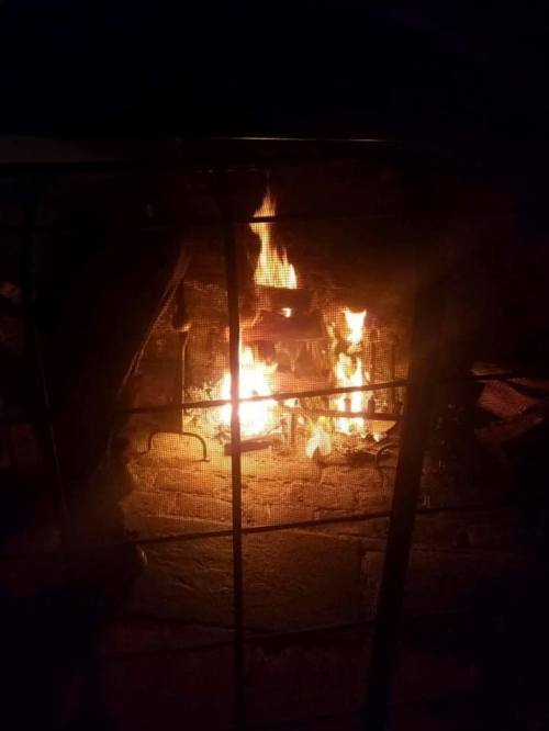 A cozy fire burns behind a metal grate, casting warm light in a darkened space.