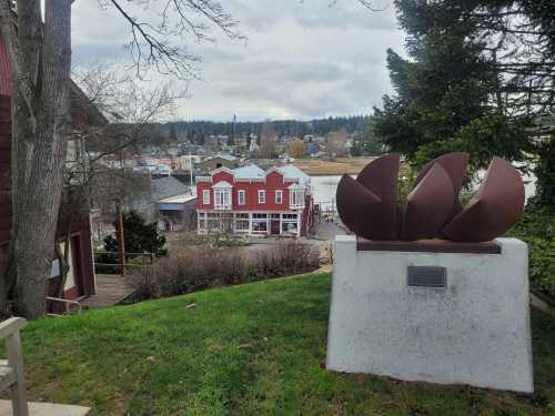 A metal sculpture in the foreground with a view of a waterfront town and cloudy sky in the background.