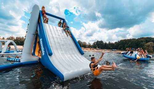 A group of people enjoying a water slide at a lake, with others playing on inflatable structures nearby.