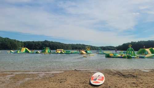 A colorful inflatable water park on a lake, with a sandy shore and a paddleboard in the foreground.