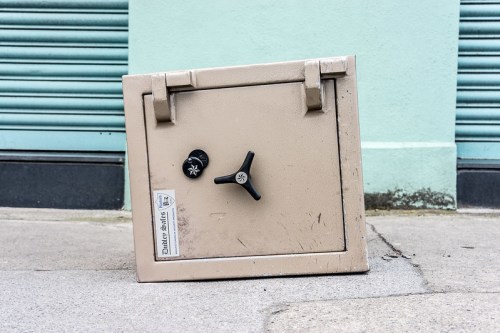 A beige safe lying on its side on a concrete surface, with a black dial and a label on the front.