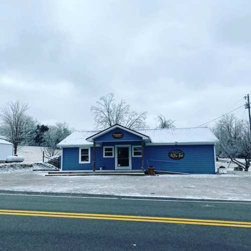 A blue house with a sign, surrounded by frosty trees and a cloudy sky, along a quiet road.