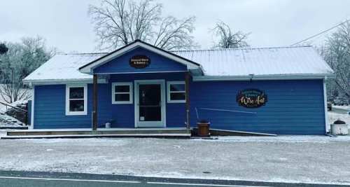 A blue building with a sign, surrounded by snow, featuring a porch and a wintery landscape.