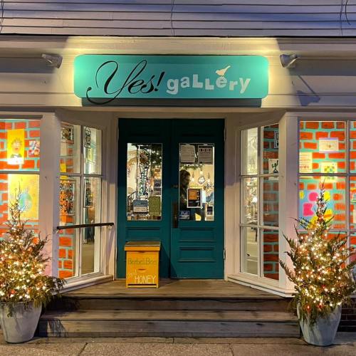 A brightly lit gallery entrance with colorful windows, festive decorations, and a sign for honey outside.