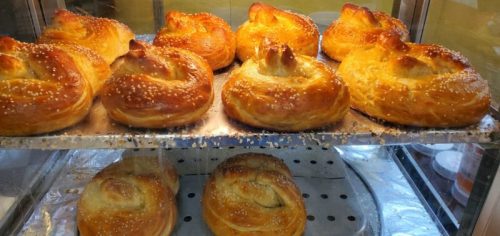 Freshly baked, golden-brown pastries with a glossy finish, topped with sesame seeds, displayed in a glass case.