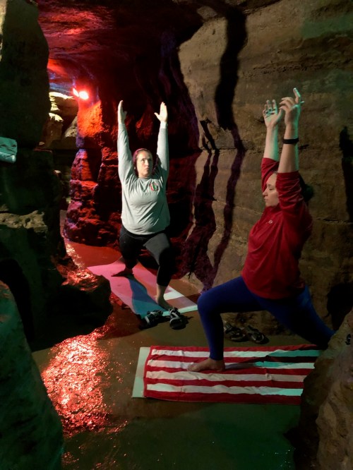 Two women practicing yoga in a cave-like setting, surrounded by rock formations and soft lighting.
