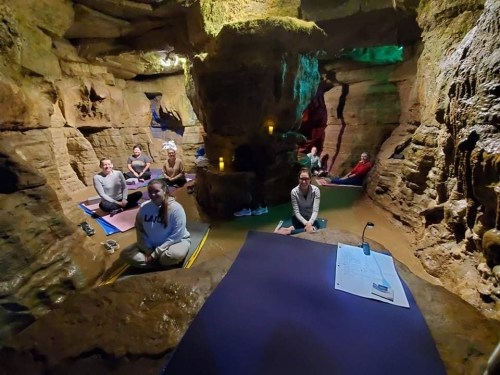 A group of people practicing yoga in a cave-like setting with soft lighting and natural rock formations.