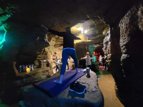 A person practicing yoga on a mat in a cave, surrounded by water and other people in a dimly lit environment.