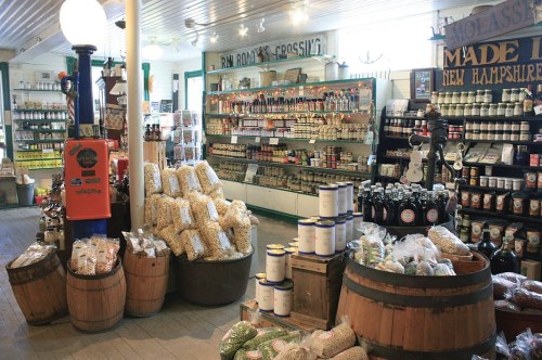 A cozy store interior filled with jars, canned goods, and barrels of grains and snacks, creating a rustic atmosphere.